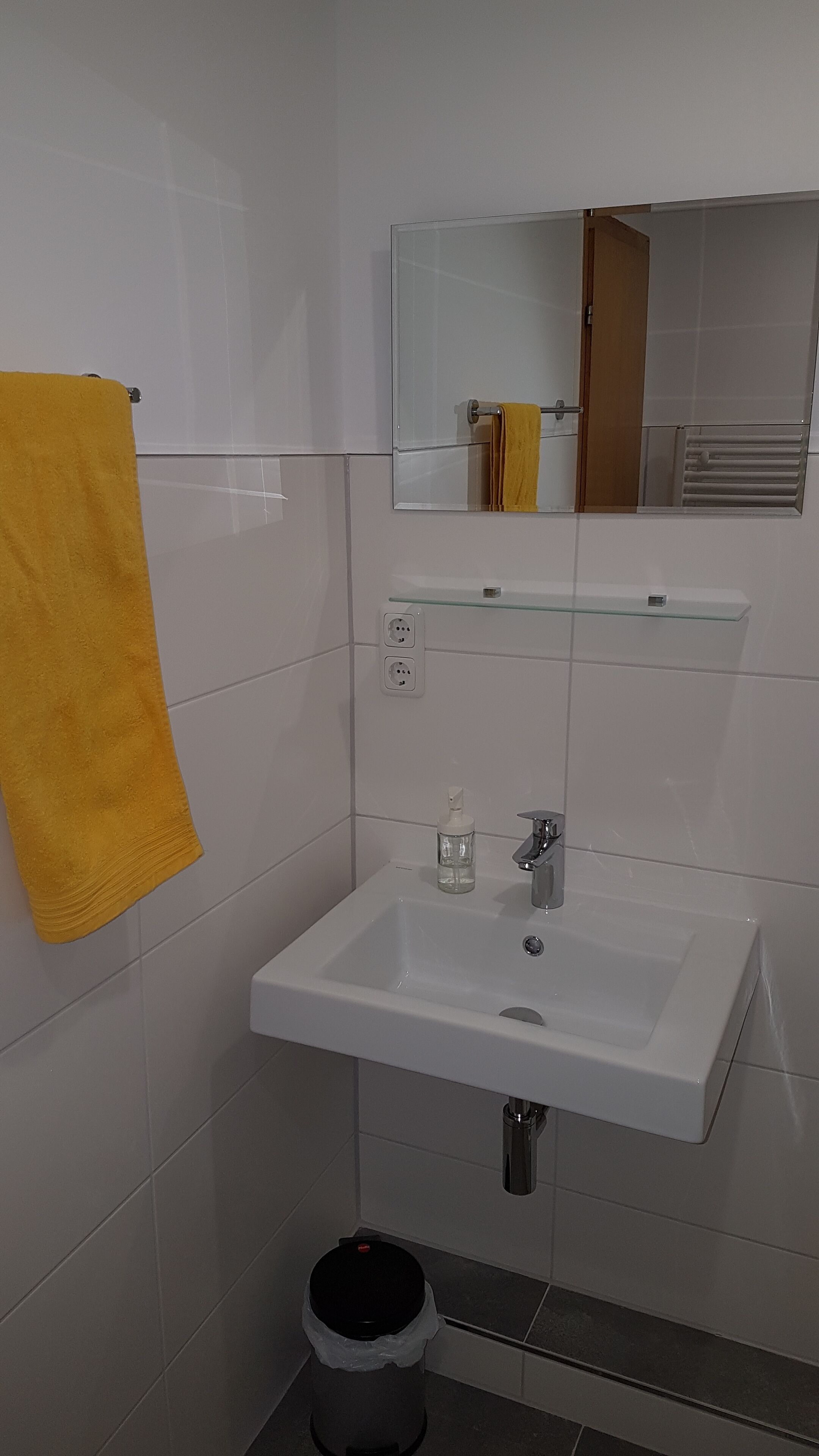 Ein Badezimmer mit einem weißen Waschbecken, einem Spiegel und einem gelben Handtuch an der Wand.