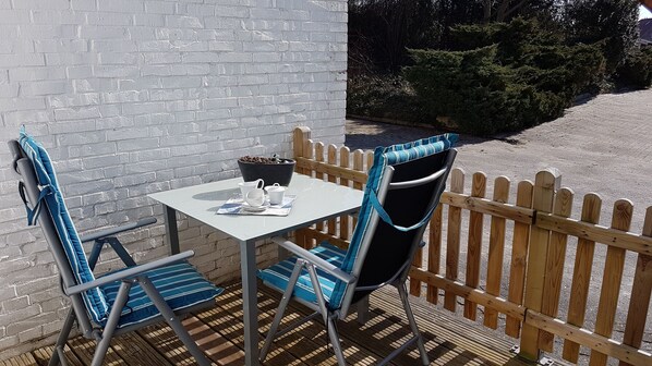 A patio with a table and chairs, a black bowl with nuts, and a wooden fence. - House (Dornum)