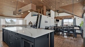 A spacious kitchen with a large island, wooden ceiling beams, and a dining area with a high table and chairs. - Domaine Des Mésanges (Beaupré)
