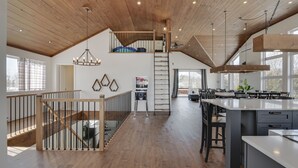 A spacious kitchen with a large island, wooden flooring, and a loft area with a staircase. - Domaine Des Mésanges (Beaupré)