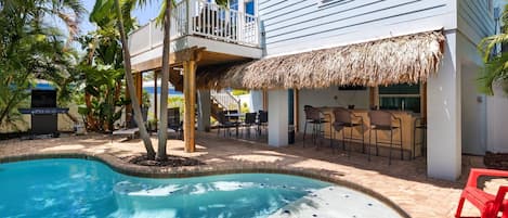 A pool area with a hot tub, outdoor seating, and a barbecue grill.