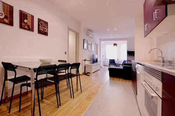 A modern kitchen with a dining area, wooden flooring, and a view into the living room.