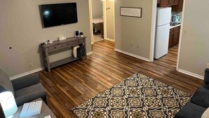 Un salon doté d’un téléviseur à écran plat, d’un canapé de couleur foncée, d’un tapis à motifs et d’un plancher en bois.