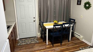 Une cuisine de taille modeste, avec une porte blanche, des placards en bois et un coin repas comprenant une table et des chaises.