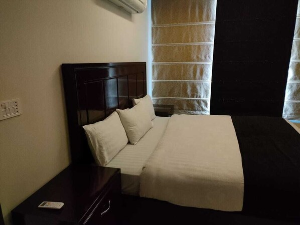A hotel room with a bed, a nightstand, and a window with curtains. - MIDWAY HOTEL & RESIDENCY (Lahore)