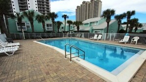 Una piscina con borde de baldosas, rodeada de sillones de descanso y palmeras.