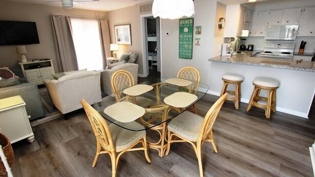 Un salón moderno con una mesa de comedor de vidrio rodeada por sillas de mimbre, un sofá y un televisor.