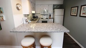 Una cocina con gabinetes blancos, encimera de granito y un lavamanos doble. Hay dos taburetes frente al lavamanos.