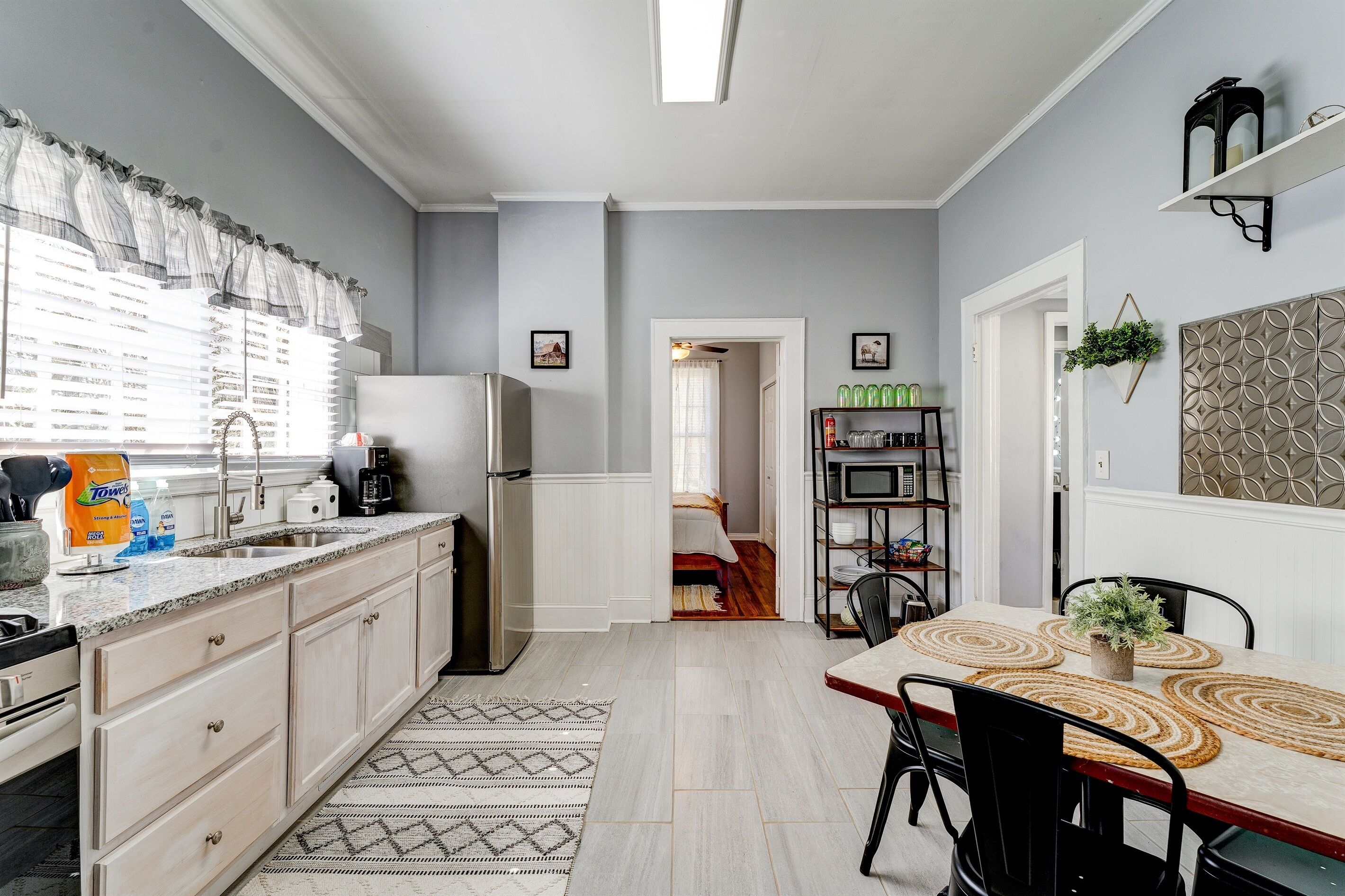A modern kitchen with a granite countertop, white cabinets, and a dining area with a wooden table and chairs.