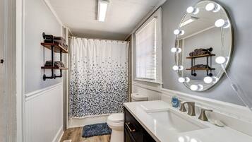 Un baño con tocador, ducha con cortina, inodoro y espejo con iluminación.