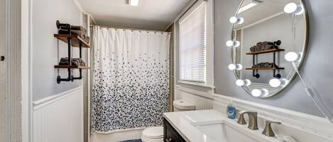 A bathroom with a vanity, a shower with a curtain, a toilet, and a mirror with lights.