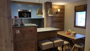 A modern kitchen with wooden accents, a central island with bar stools, pendant lighting, and a window with curtains. - 230m from ski slopes, floor -3, view mountain, balcony, 44m², Méribel-Mottaret (Méribel - Les Allues)