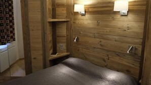 A wooden-paneled room with a bed, two wall-mounted lights, and a small shelf. - 230m from ski slopes, floor -3, view mountain, balcony, 44m², Méribel-Mottaret (Méribel - Les Allues)