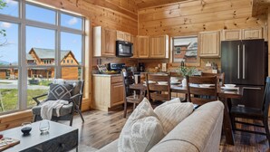 Eine gemütliche Küchenzeile im Chalet-Stil mit Holzwänden und großen Fenstern, mit einer Essecke mit Tisch und Stühlen sowie einer Couch im Vordergrund.