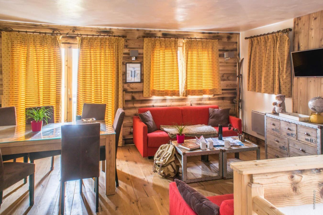 Een gezellig houten kamer, ingericht als een blokhut, met een rode bank, een eettafel met stoelen en een kleine salontafel.