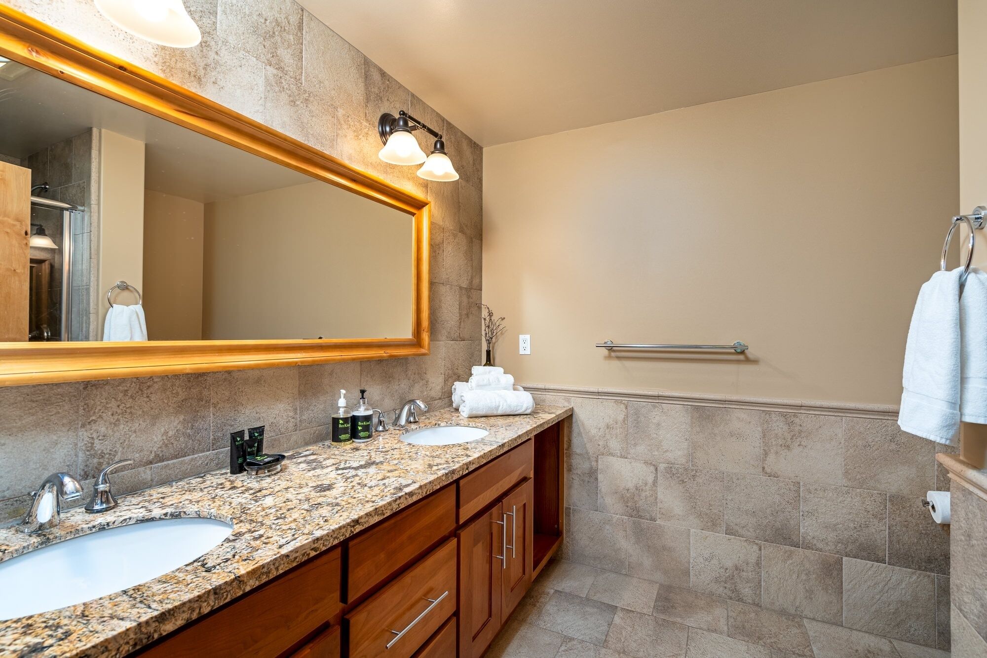 A modern bathroom with granite countertops, a large mirror, and a walk-in shower.