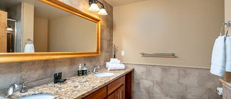 A modern bathroom with granite countertops, a large mirror, and a walk-in shower.