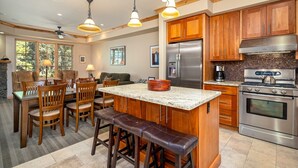 A spacious kitchen with wooden cabinets, a stainless steel refrigerator, a double oven, and a granite countertop. There are wooden chairs and a bench around the island.