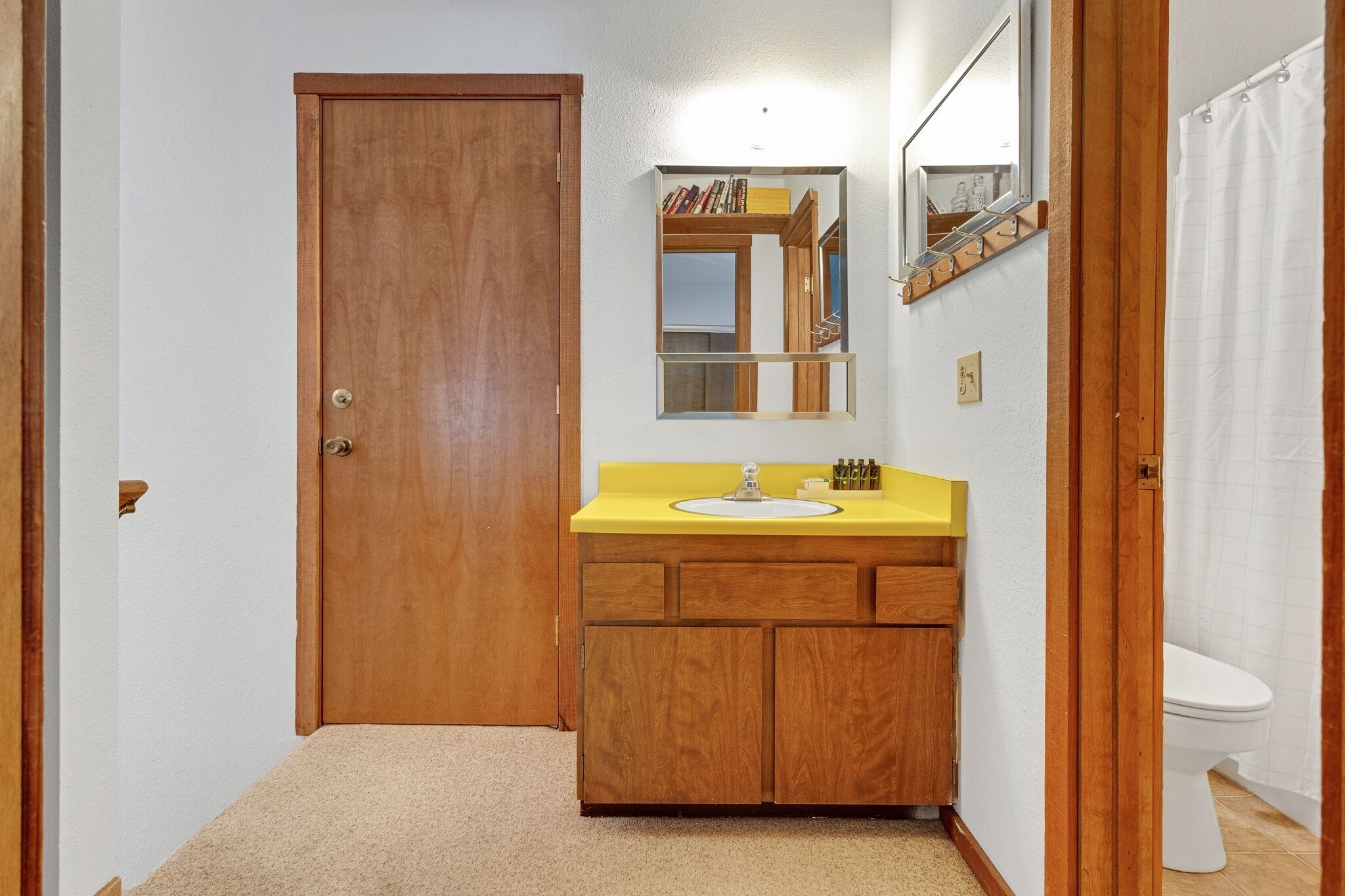 Une salle de bain avec une porte en bois, un meuble-lavabo jaune, un miroir et des toilettes blanches.