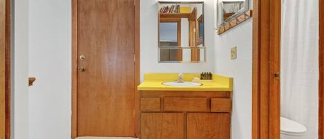 Une salle de bain avec une porte en bois, un meuble-lavabo jaune, un miroir et des toilettes blanches.