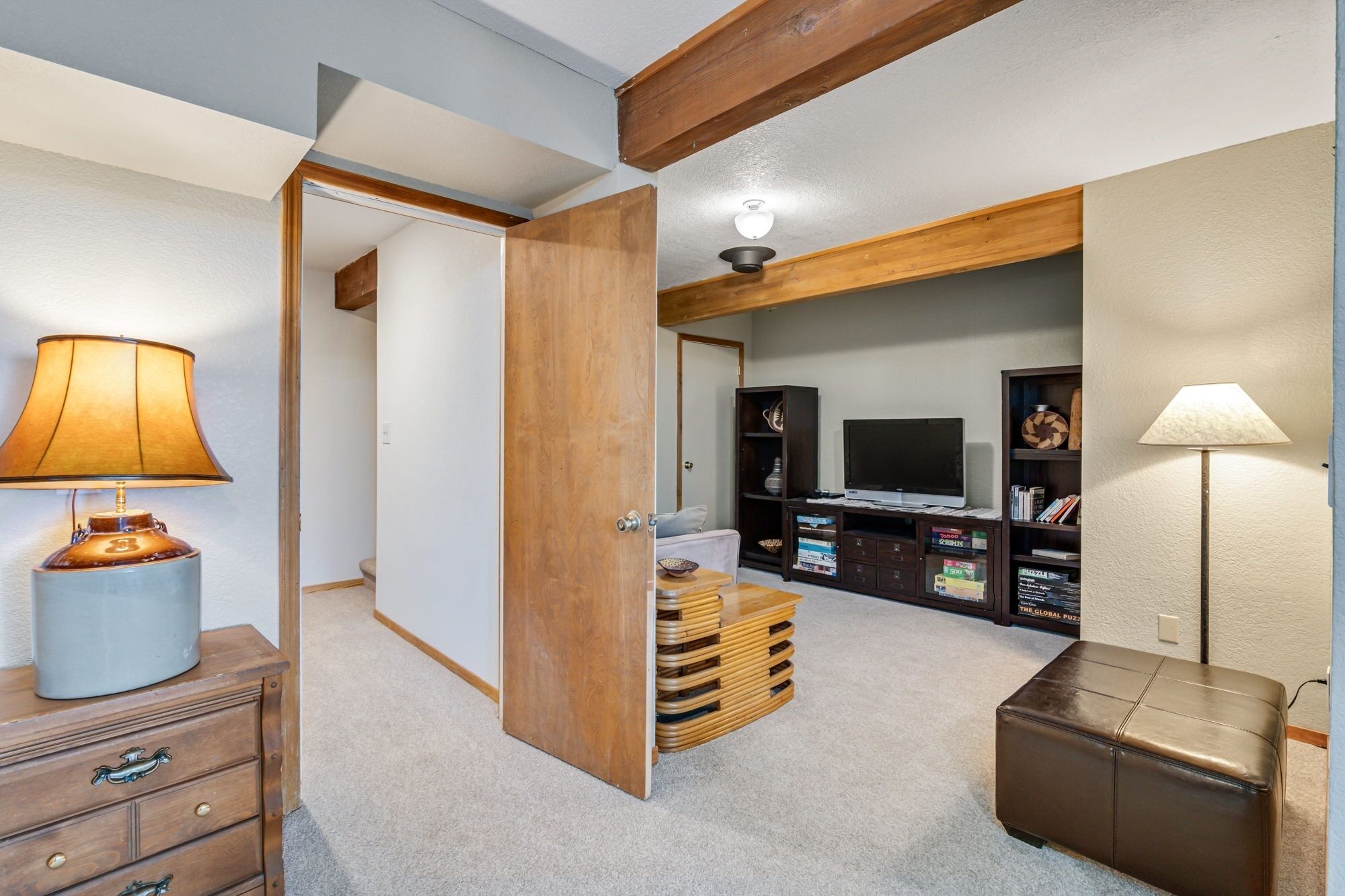 A room with a wooden door, a TV stand with a flat-screen TV, a lamp, and a stack of wooden crates.