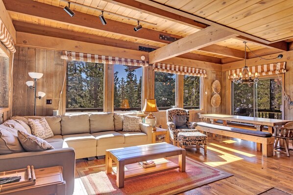 A cozy cabin interior with a wooden ceiling, large windows, a sofa, a table, and a bench. - Overlooking Beautiful Bear Lake VH#318 by Bear Valley Vacation Rentals (Arnold)