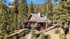 A wooden cabin with a balcony, surrounded by dense forest. - Overlooking Beautiful Bear Lake VH#318 by Bear Valley Vacation Rentals (Arnold)