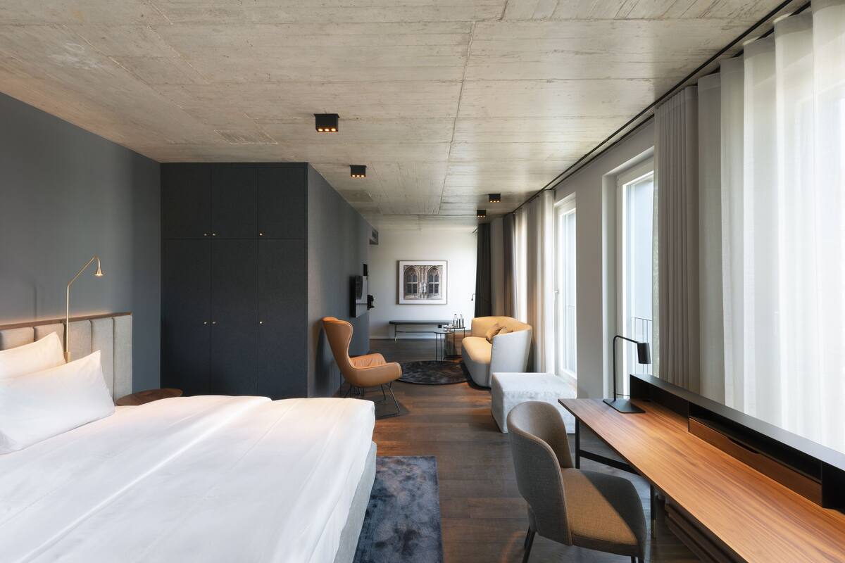 A modern hotel room with a large bed, a desk, and a seating area.