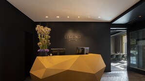 A reception desk with a geometric design, a vase of flowers, and a wall-mounted sign. - Legend Hotel (Cologne)