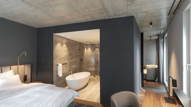 A modern bedroom with a large bed, a sitting area, and a view of the bathroom. - Legend Hotel (Cologne)