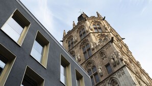A modern building with large windows and a historic building with intricate stonework and statues in the background. - Legend Hotel (Cologne)