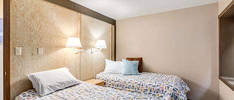 A hotel room with two beds, each with patterned bedding, a wooden headboard, and wall-mounted lamps.
