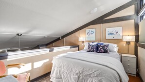 Un dormitorio con cama, mesitas de noche, decoración en la pared y una ventana.