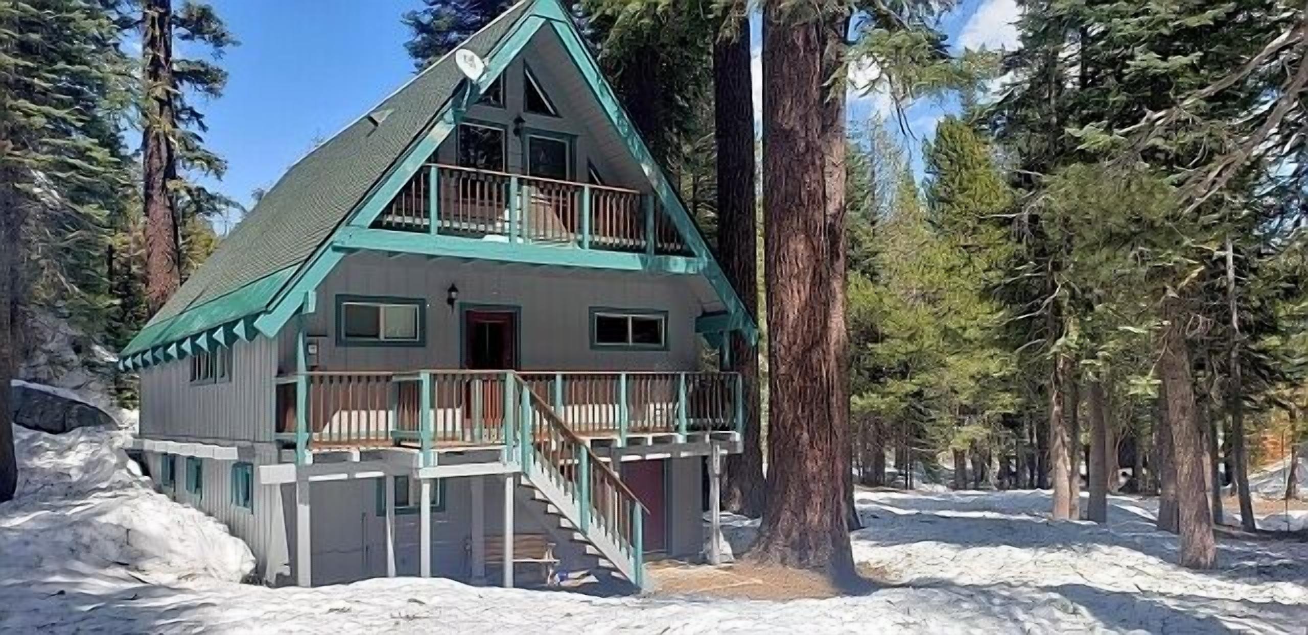 Eine zweistöckige Holzhütte mit Balkon, umgeben von Schnee und hohen Bäumen.