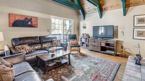 A cozy living room with a leather sofa, a coffee table, a TV, and a bookshelf. - Multi-Family Cabin in Great Location! - Home #183 by Bear Valley Vacation Rentals (Arnold)