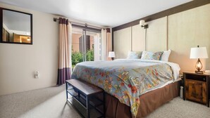 A bedroom with a bed, bench, bedside table, lamp, and a window with curtains.