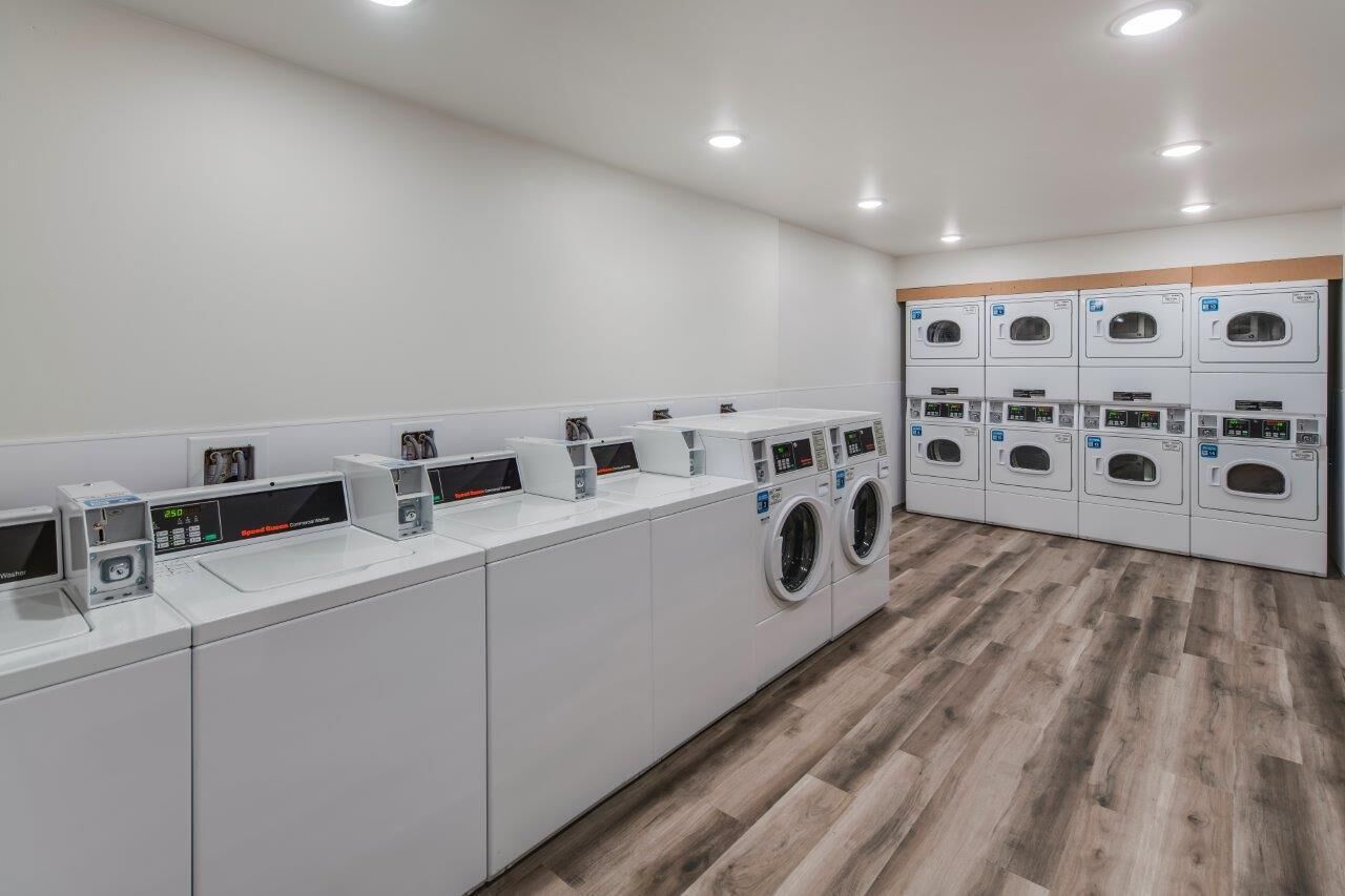 Een moderne wasserette met meerdere wasmachines en drogers, een digitaal bedieningspaneel en een houten vloer.