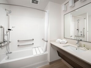 A modern bathroom with a walk-in shower, grab bars, a sink with a mirror, and neatly folded towels.