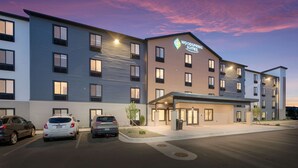 A modern hotel with a flat roof, multiple windows, and a parking lot with several cars.