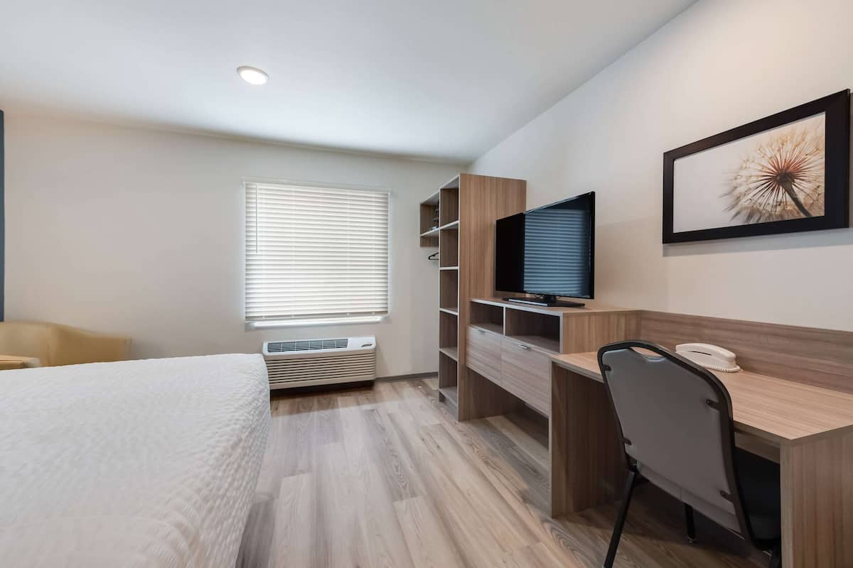 Ett modernt hotellrum med en säng, ett skrivbord, en stol, en tv och ett inramat konstverk på väggen.
