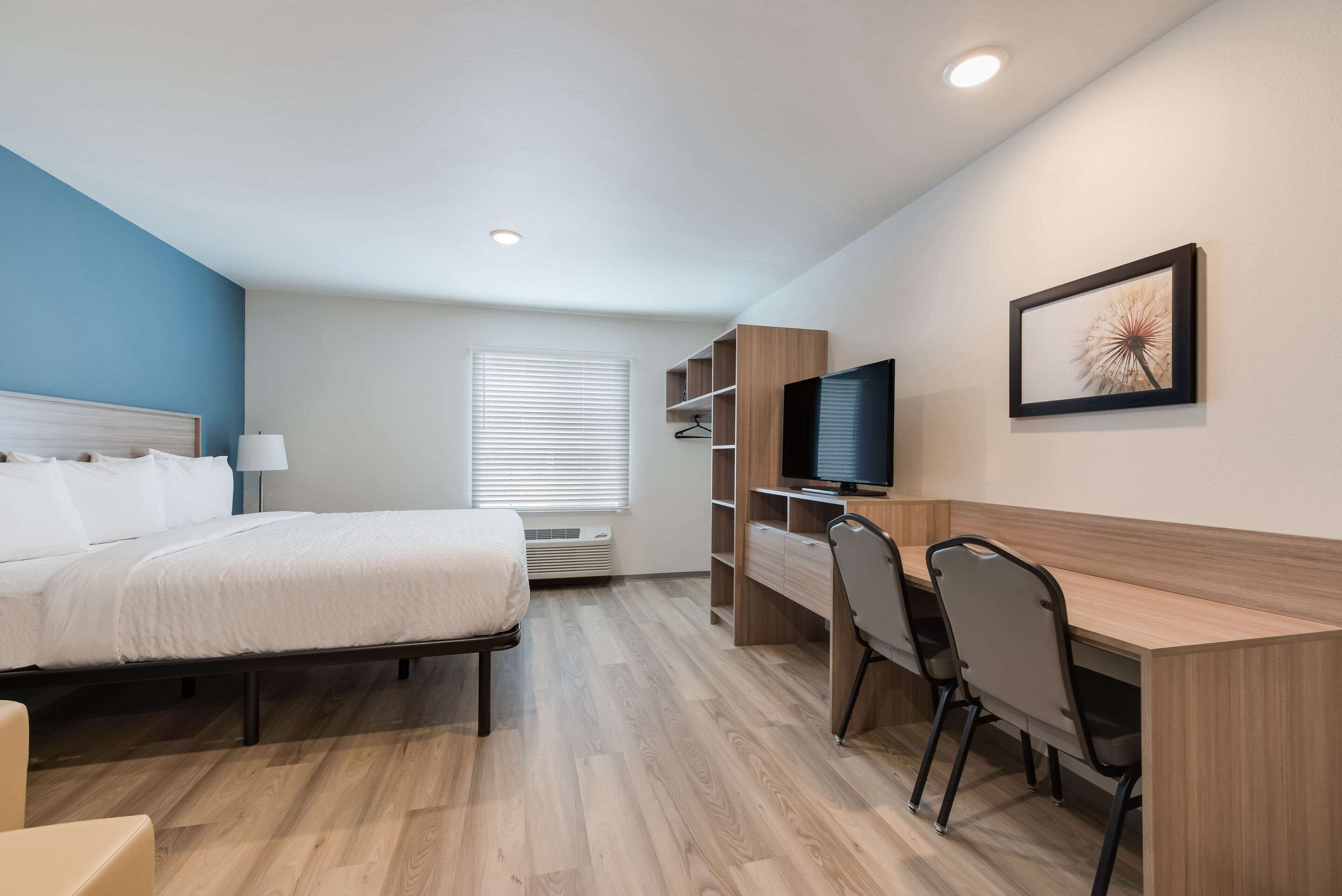 A hotel room with a bed, desk, chairs, a TV, and a window with blinds.