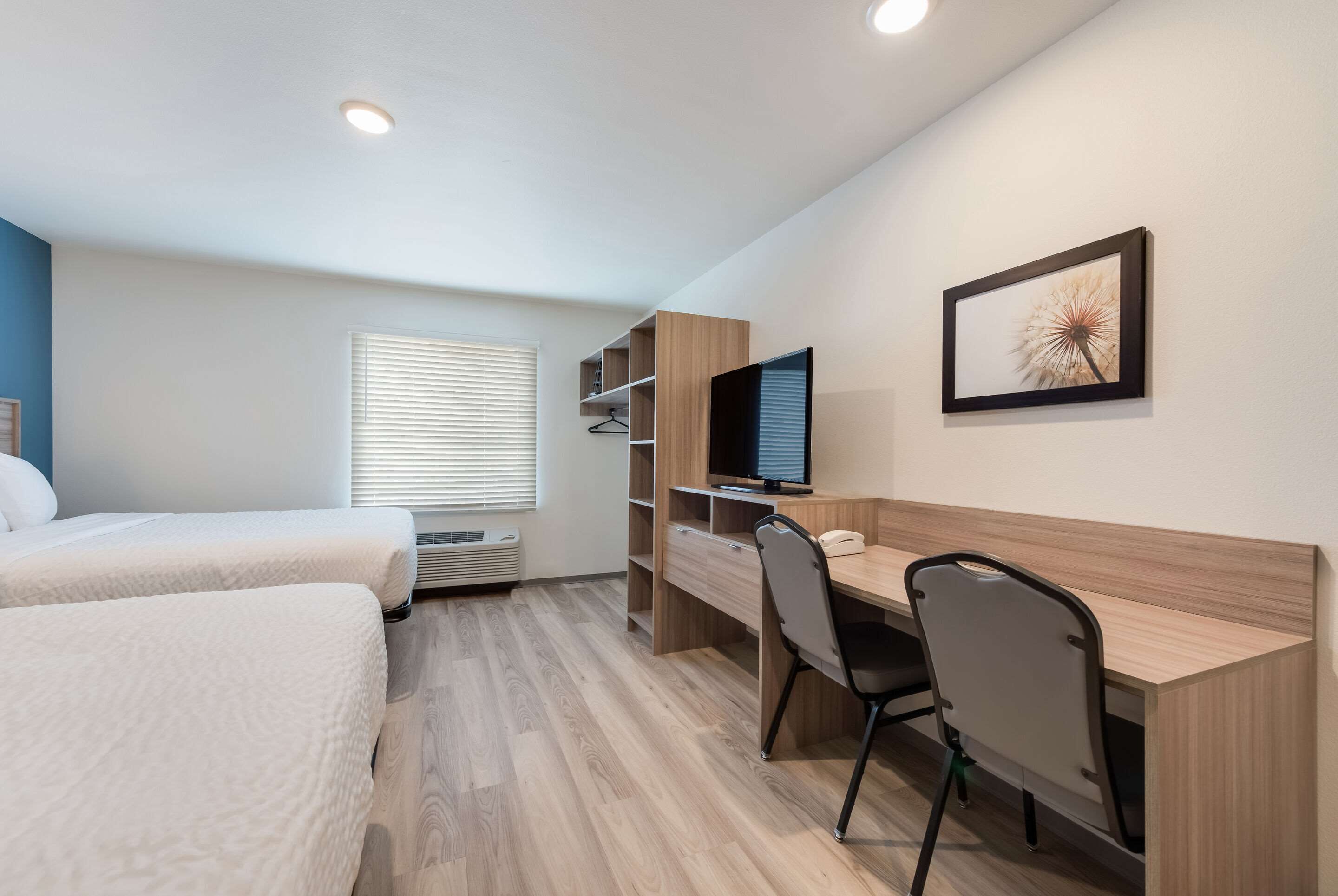 A bedroom with two beds, a desk with a chair, a TV, and a framed picture on the wall.