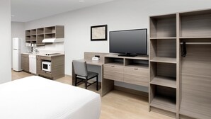 A modern hotel room with a bed, a desk with a chair, a TV, and built-in shelving.