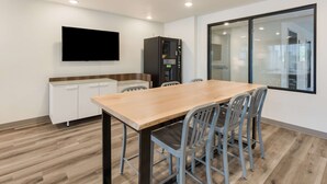 A modern kitchen with a wooden table and chairs, a built-in oven, and a flat-screen TV mounted on the wall.