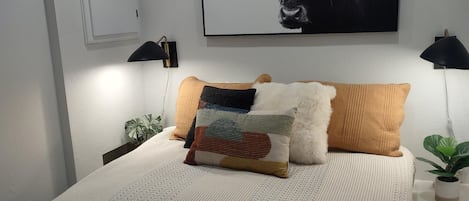 Une chambre à coucher avec un lit, des oreillers, une œuvre d’art représentant un taureau accrochée au mur, des lampes de chevet et une plante en pot.