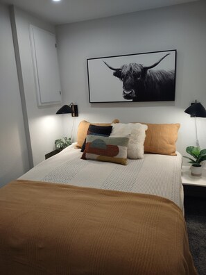 A bedroom with a bed, pillows, a wall-mounted artwork of a bull, bedside lamps, and a potted plant.
