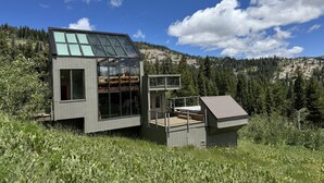 A modern house with a glass facade, wooden deck, and a view of a forested mountain. - Stunning! Enjoy The Best Views In All Of Bear Valley When You Stay At This Unique Property 3 Bedroom Apts by RedAwning (Arnold)