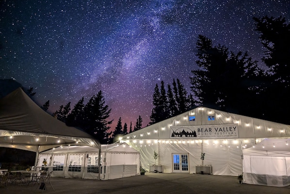 A tented event space with a starry night sky, a marquee with 'Bear Valley Music Festival' signage, and a mountainous backdrop.