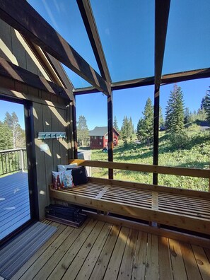 A wooden deck with a bench, a window, and a view of a forest and buildings.