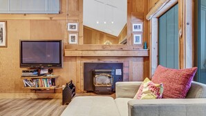 A cozy living room with a flat-screen TV, a fireplace, a sofa, and a bookshelf. - Modern & Sleek Condo - Creekside #110 by Bear Valley Vacation Rentals (Arnold)